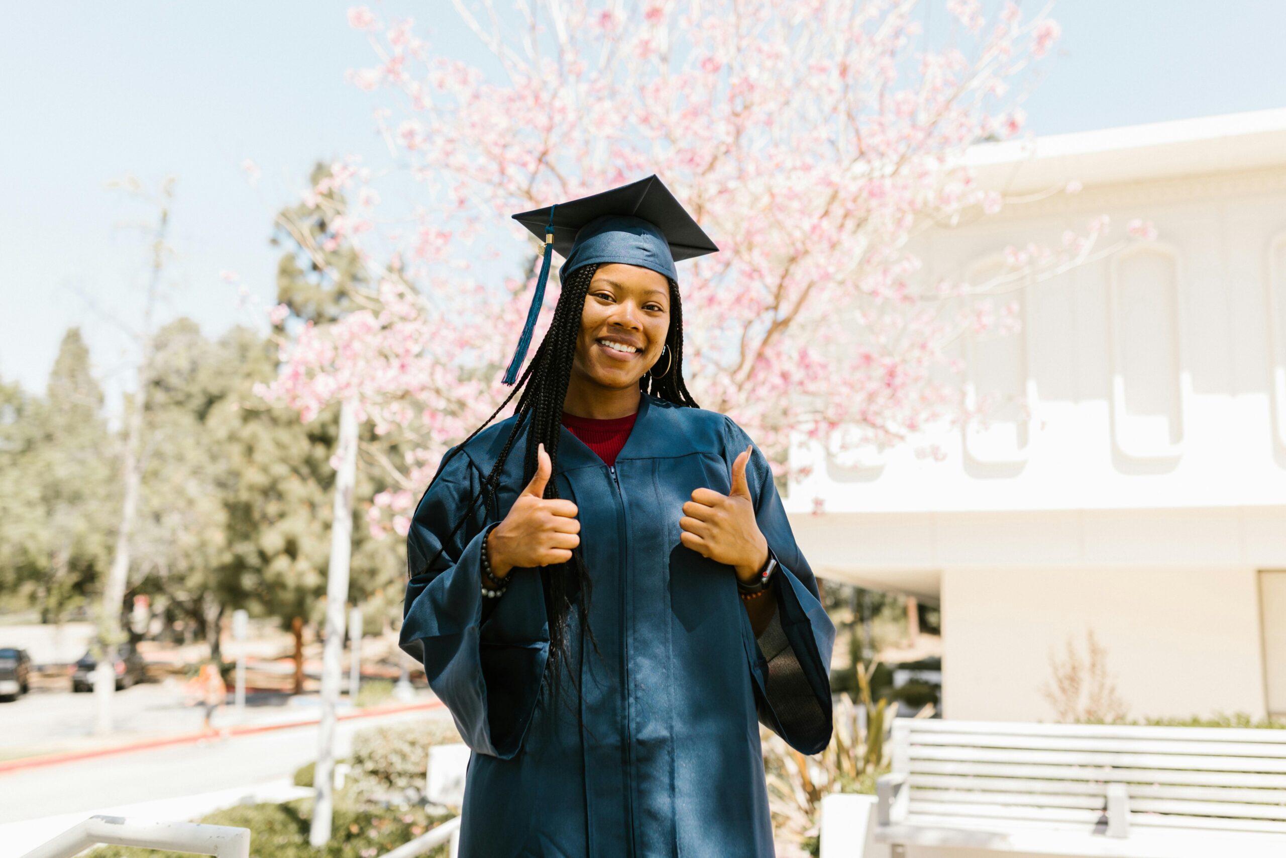 Academic tutoring UK – smiling young woman in graduation cap giving a thumbs up, celebrating academic success.